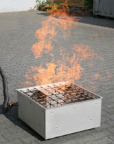 Eine Feuerquelle mit Flammen steht auf einem grauen Pflastersteinboden während einer Brandschutzunterweisung.